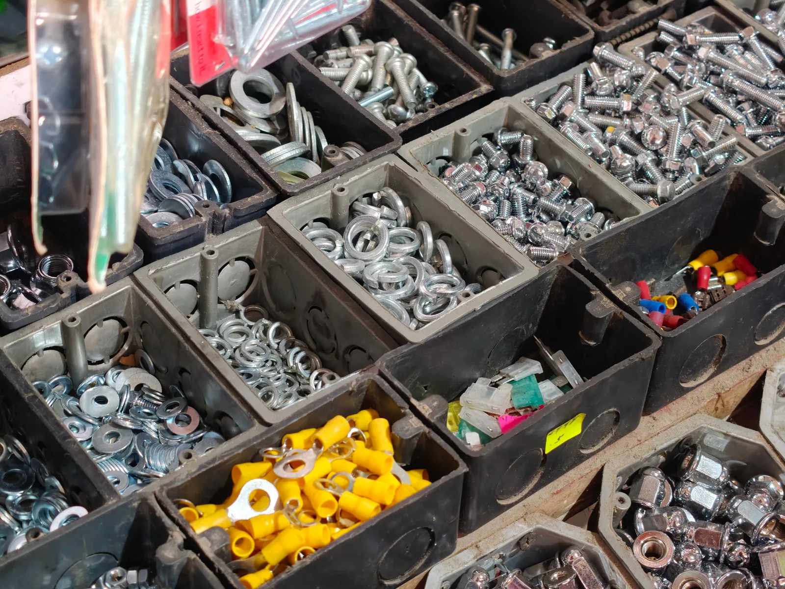Close-up view of various hardware fasteners in black storage bins, including nuts, bolts, and washers. Electrical Contractor Van Stock Inventory List That Keeps Techs Moving