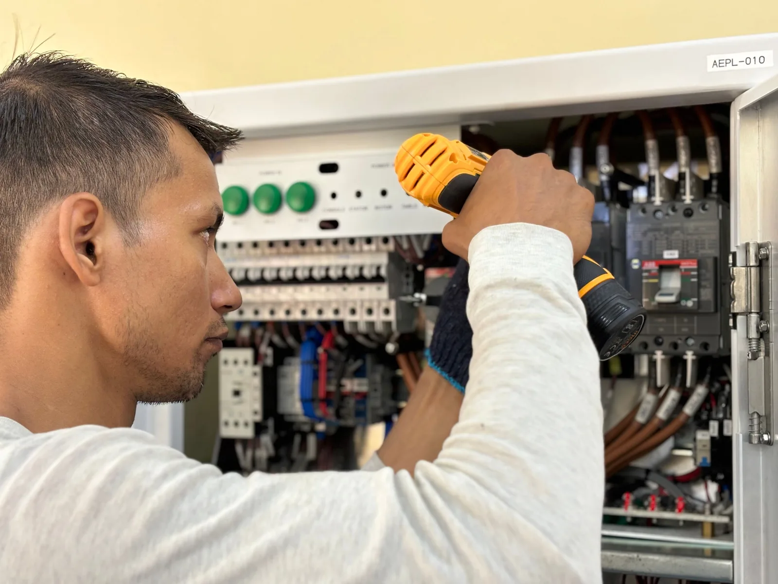 Professional electrician using a drill on an indoor circuit breaker panel. Start an electrical contractor business: when to add each role